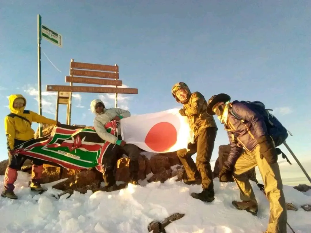 Group of trekkers celebrating with flags at the Point Lenana summit sign